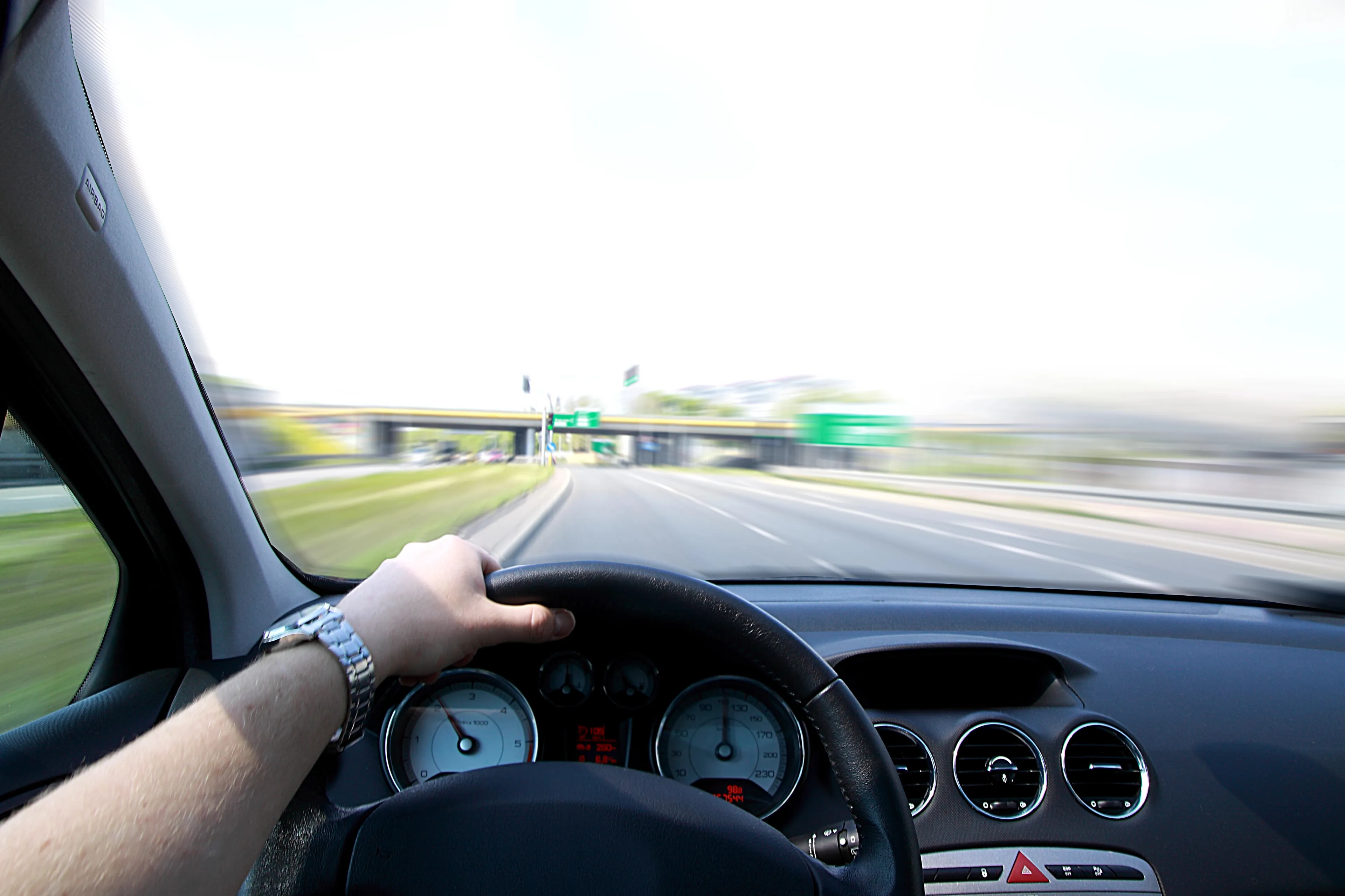 Bild zeigt das Cockpit eines Autos mit am Hand des Fahrers am Lenkrad, der auf der linken Spur der Autobahn fährt.