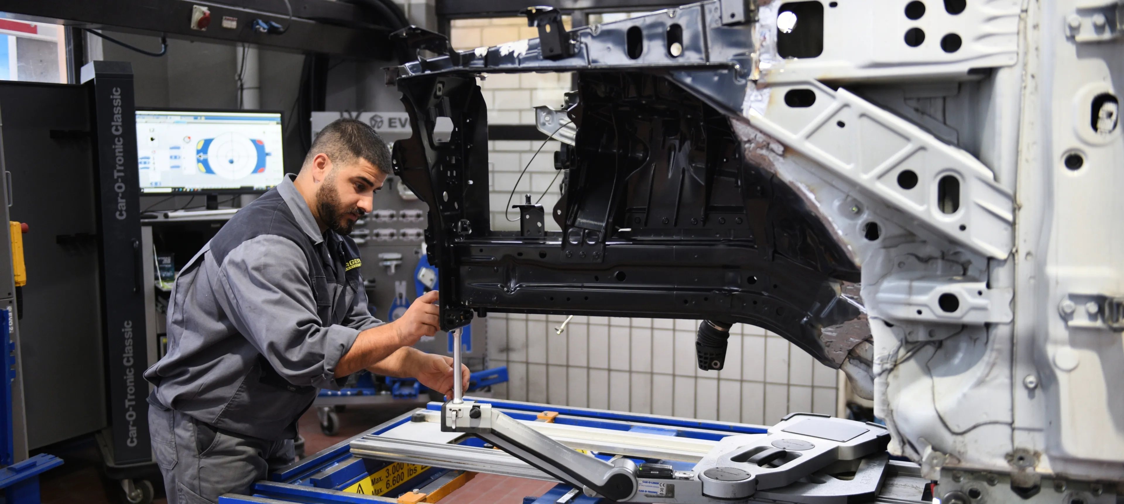 Auf dem Bild ist ein Mechaniker zu sehen, der an einem Fahrzeug eine Vermessung macht.