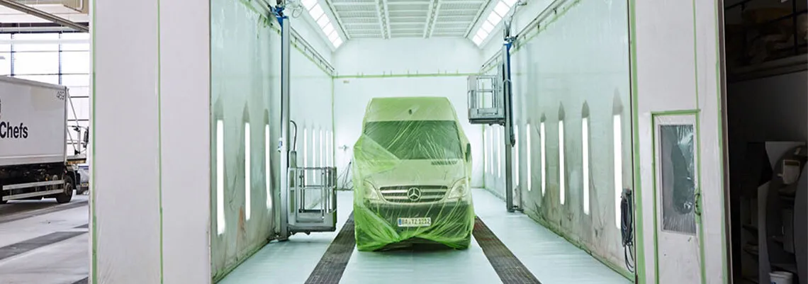 Das Bild zeigt einen Transporter, der mit Folie abgeklebt ist, in der großen Lackierhalle für LKWs, Busse und andere Großfahrzeuge