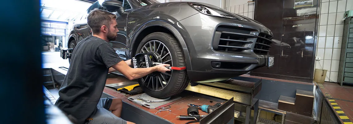 Es ist ein Mitarbeiter zu sehen, der die Spureinstellung eines Fahrzeugs auf der Richtbank kontrolliert