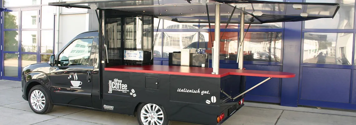 Bild zeigt einen umgebauten Lieferwagen zum Kaffemobil mit aufklappbaren Seitenwänden zum Schutzdach und Fläche für Kaffeautomaten zur Getränkeausgabe